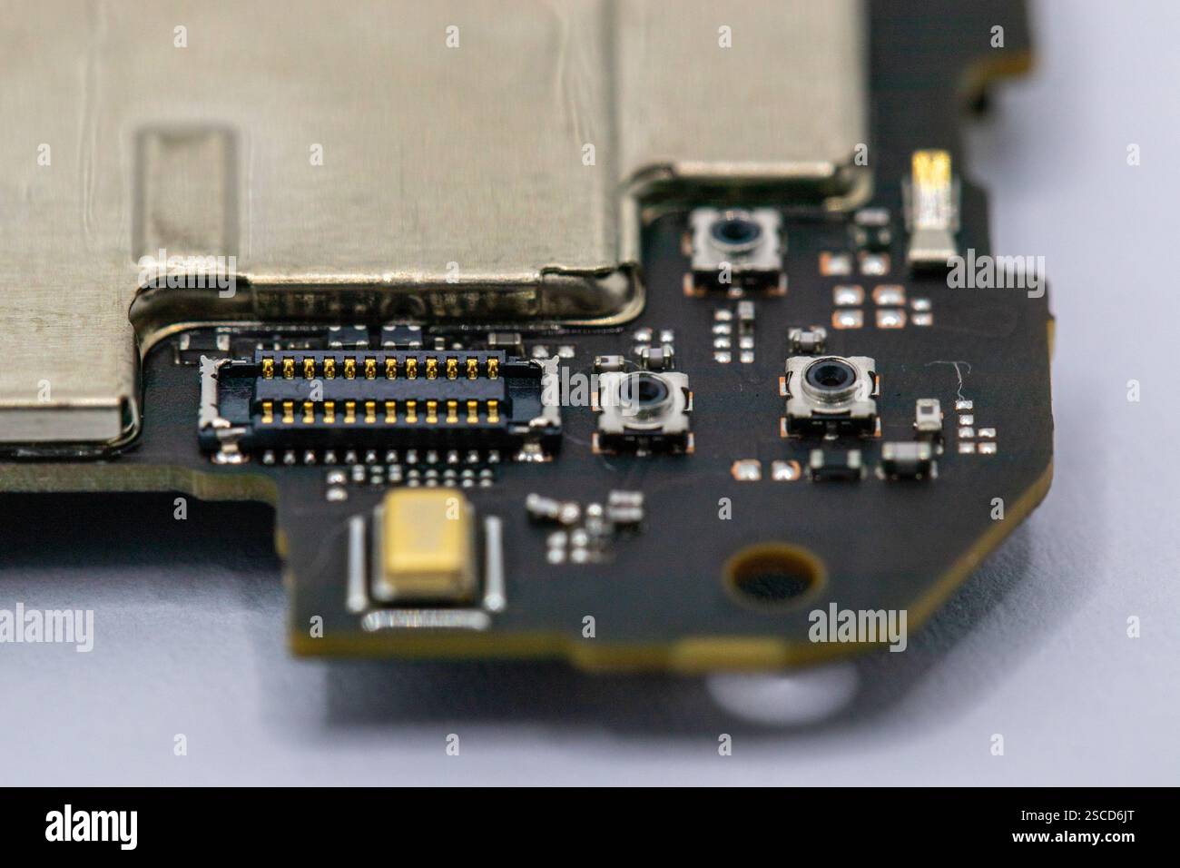 Vue rapprochée d'un fragment de carte de circuit imprimé, présentant des connecteurs en or, des composants à montage en surface et de petits commutateurs. La planche est principalement dark-c Banque D'Images