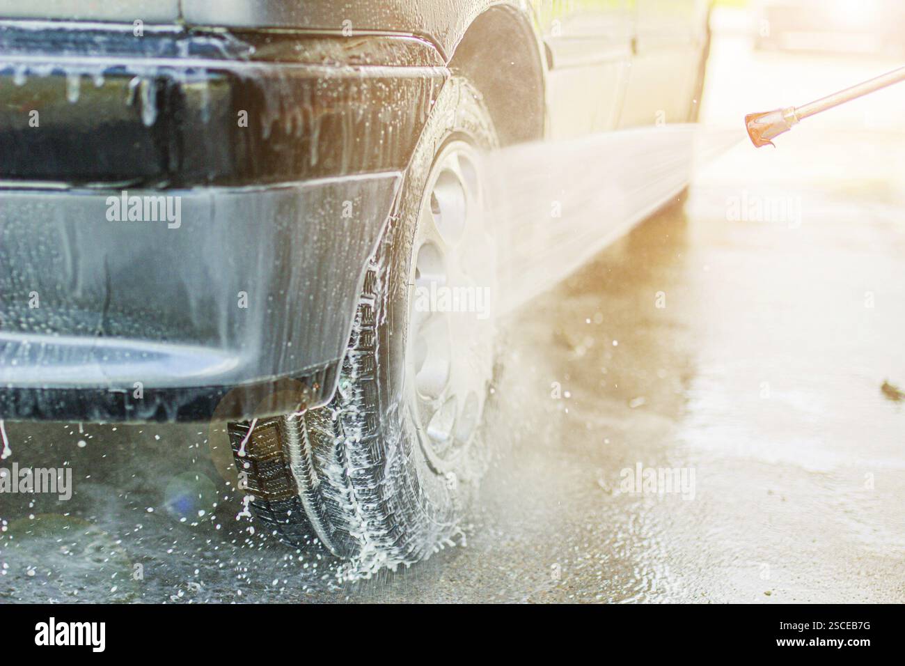 Une roue de voiture étant nettoyée avec de l'eau savonneuse et la lumière du soleil dans un lavage de voiture Banque D'Images