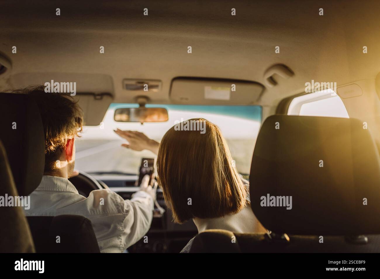 Couple à l'intérieur d'une voiture, femme faisant des gestes tandis que l'homme conduit au coucher du soleil Banque D'Images