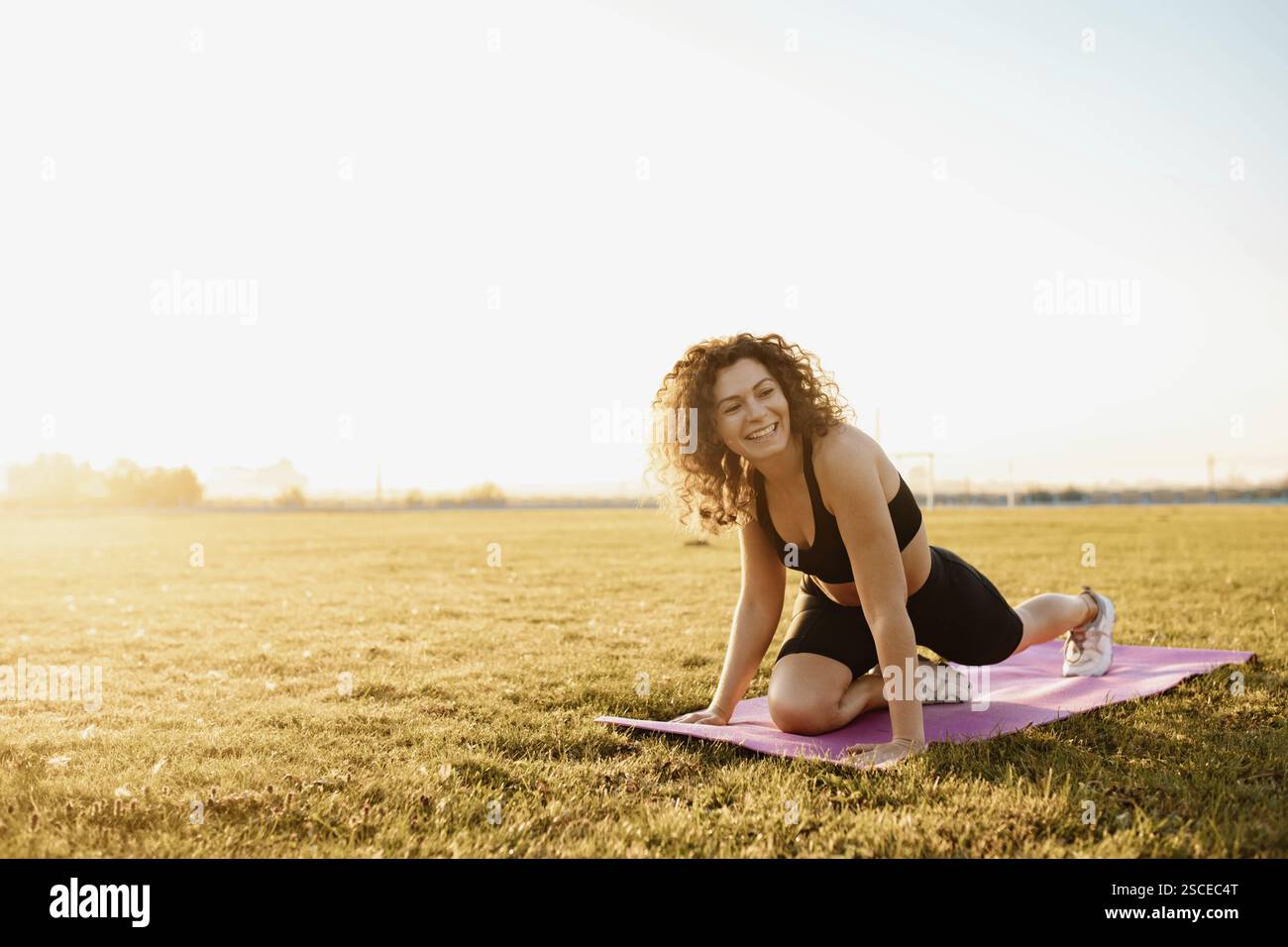 Femme souriant tout en faisant du yoga sur un tapis dans un champ lumineux Banque D'Images