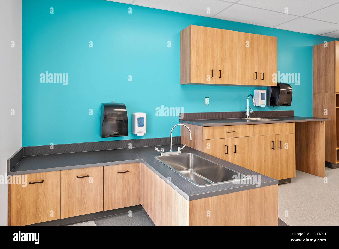 Une cuisine avec un mur bleu et des armoires en bois. L'évier est argenté et le comptoir est noir Banque D'Images