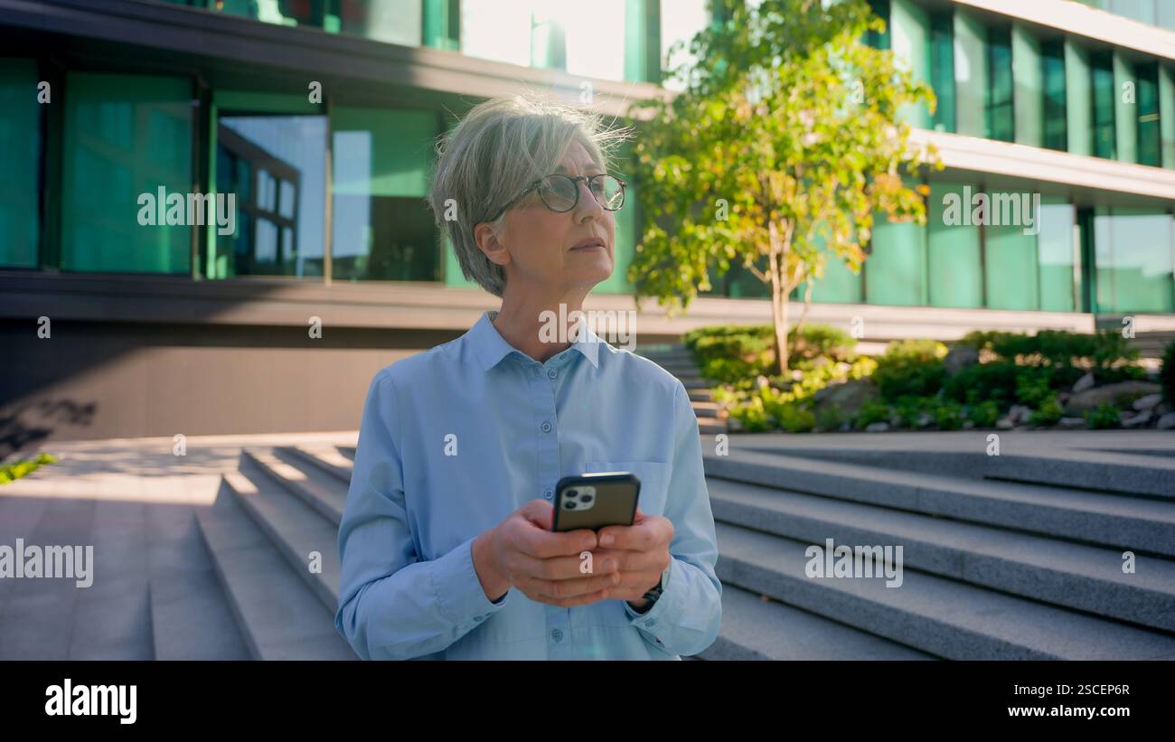 Réfléchie femme d'affaires mature aux cheveux gris des années 50 femme caucasienne senior femme tenir le téléphone pensant taper le message mobile chat messagerie entreprise mondiale Banque D'Images