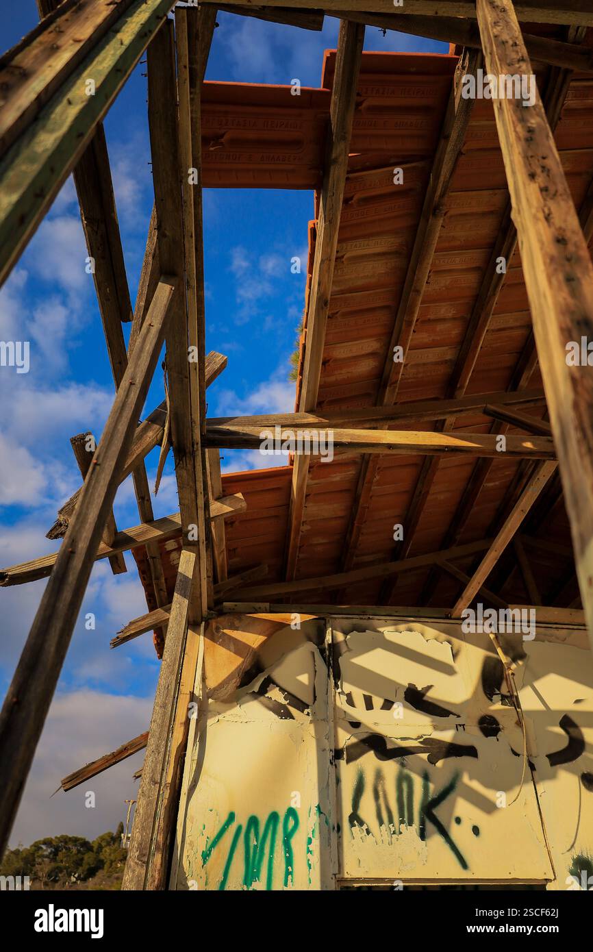 Structure de toit en bois endommagée avec tuiles en terre cuite et mur couvert de graffitis contre un ciel partiellement nuageux. Banque D'Images