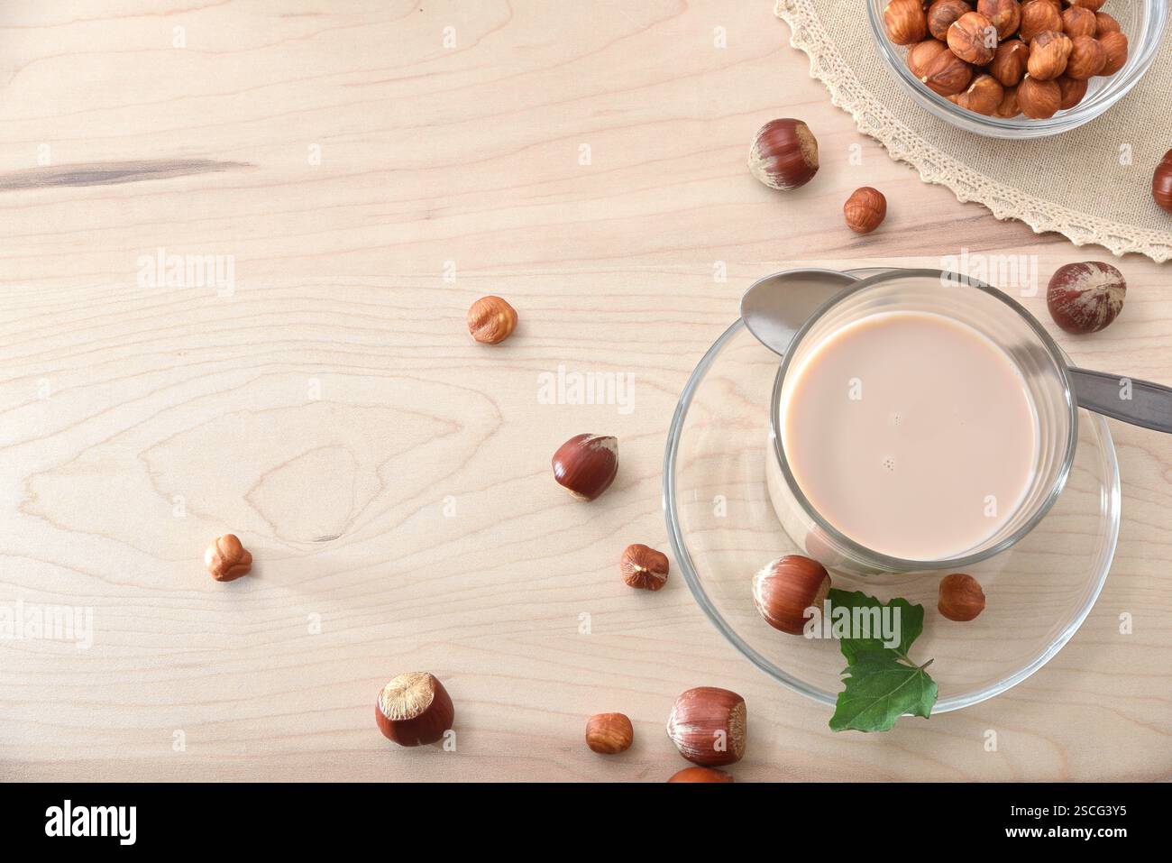 Boisson de noisette dans un verre sur un banc de cuisine en bois avec des noix et des feuilles autour. Vue de dessus. Banque D'Images