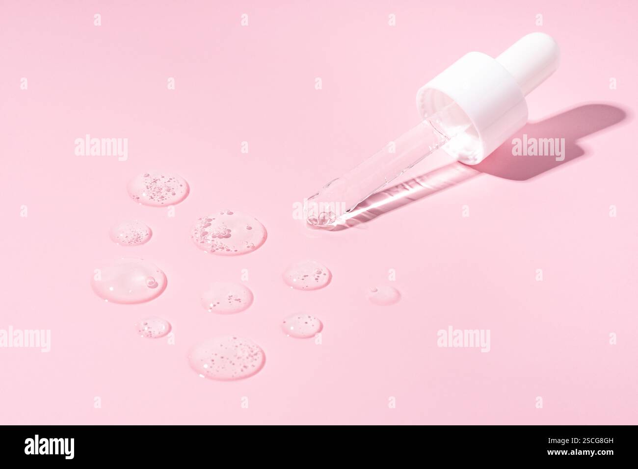 Une pipette de flacon compte-gouttes sur un sérum transparent frottis, échantillons, gouttes sur un fond rose Banque D'Images