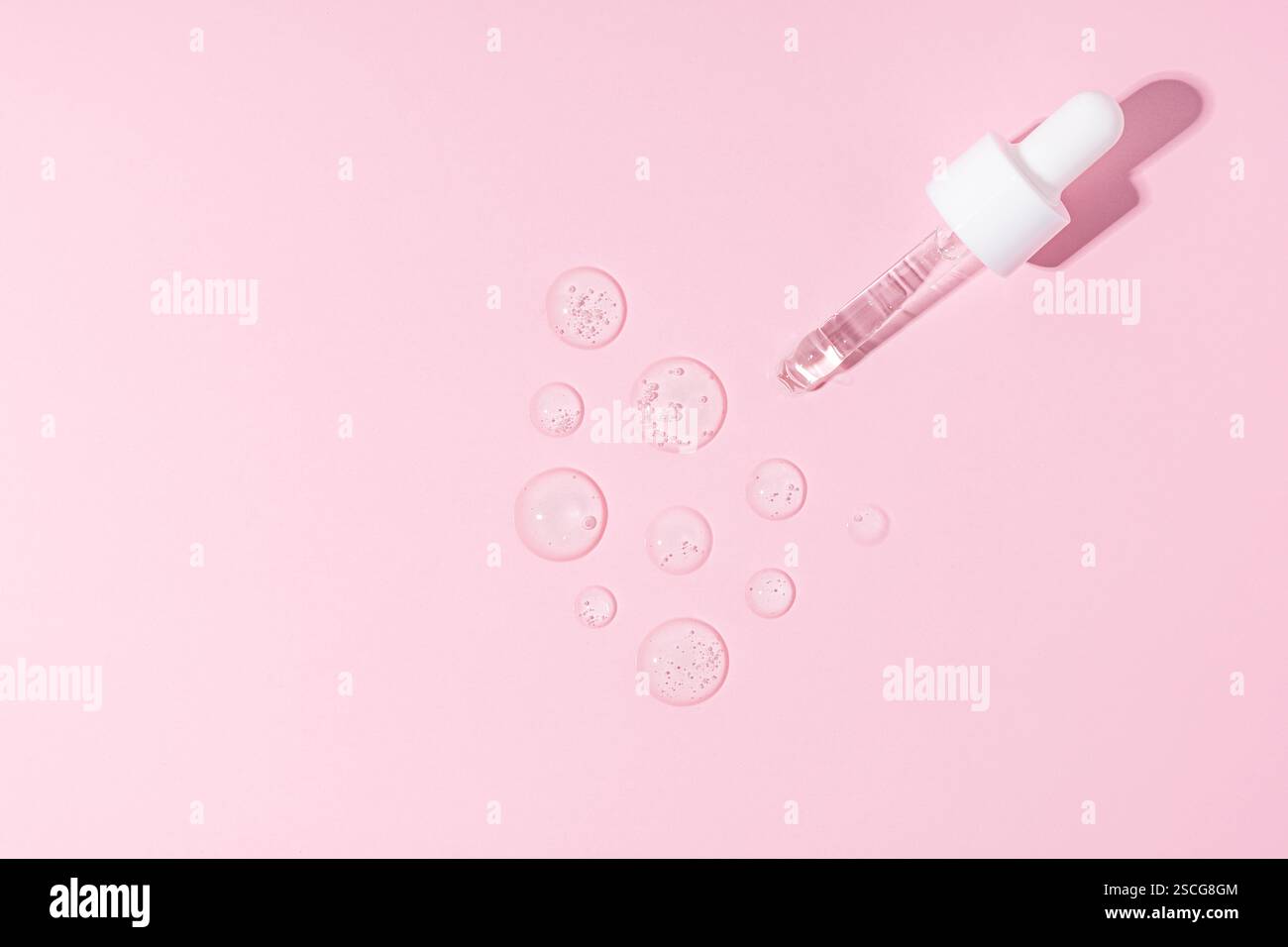 Une pipette de flacon compte-gouttes sur un sérum transparent frottis, échantillons, gouttes sur un fond rose Banque D'Images