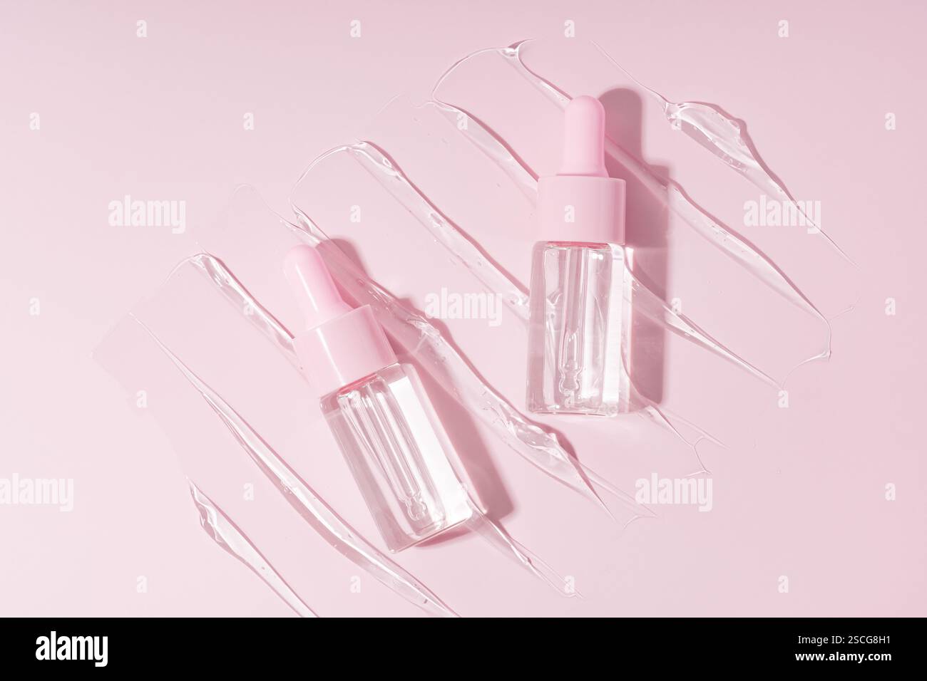 Deux flacons compte-gouttes avec pipettes sur un gel transparent sérum frottis, des échantillons sur un fond rose Banque D'Images