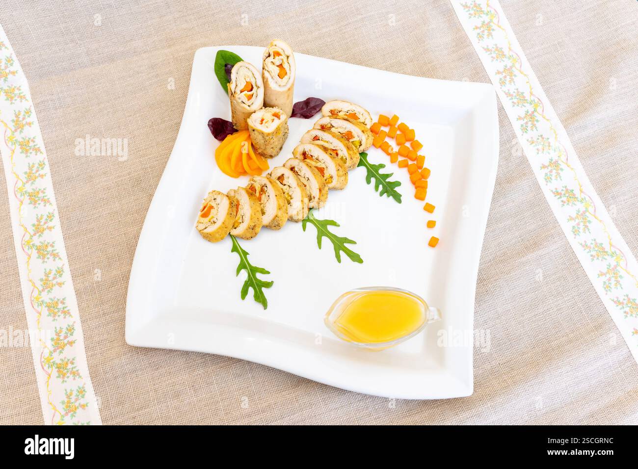 Un plat gastronomique soigneusement arrangé comprend des tranches de poulet roulées avec des garnitures vibrantes sur une assiette blanche. La présentation artistique met en valeur Freshne Banque D'Images