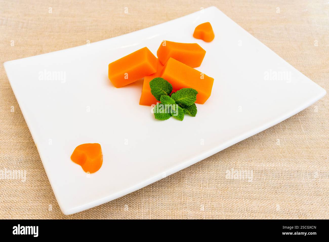 Les morceaux de dessert de melon orange vif sont artistiquement disposés sur une assiette blanche propre. Les feuilles de menthe fraîches améliorent la présentation, créant un rafraîchissement Banque D'Images