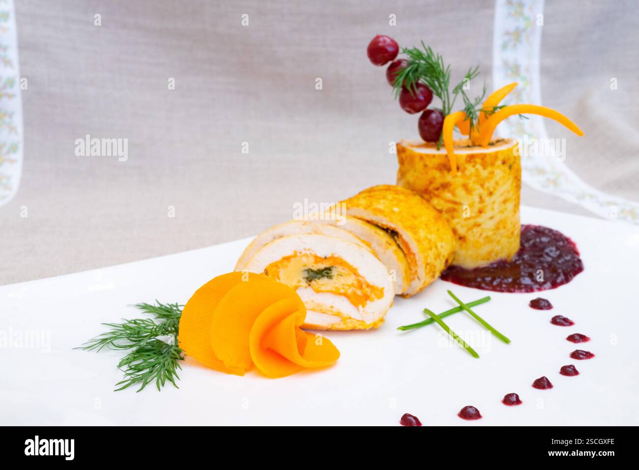 Un petit pain de poulet gastronomique magnifiquement arrangé est servi avec des garnitures vibrantes. Le plat comprend du poulet tranché rempli d'ingrédient orange et vert Banque D'Images