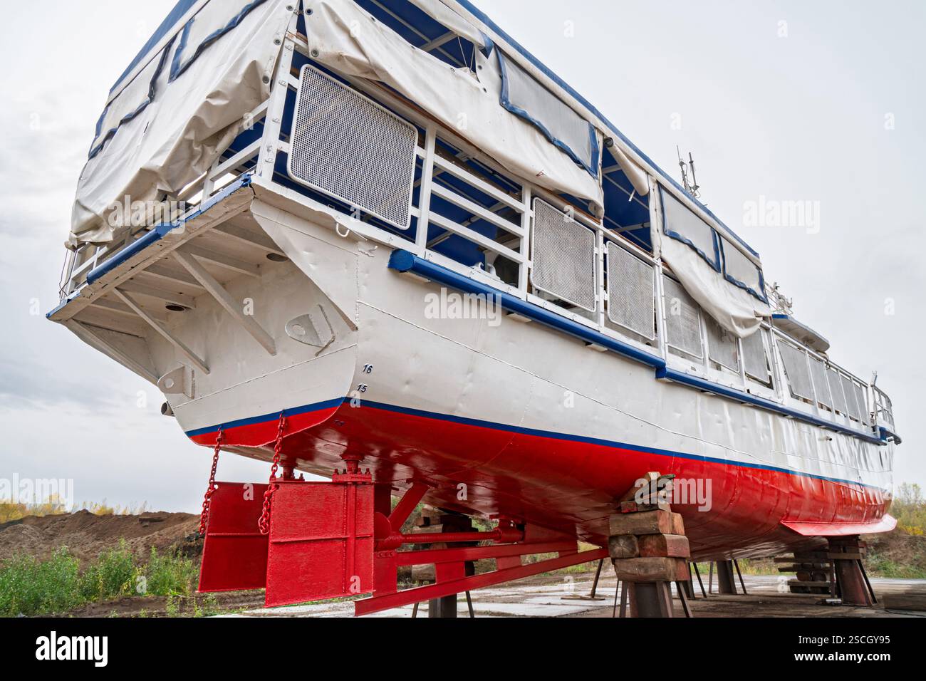 Poupe de grand bateau sur des supports en bois pour réparation sur cale sèche, avec pont supérieur couvert et garde-corps en métal, vue à angle bas contre le ciel nuageux Banque D'Images