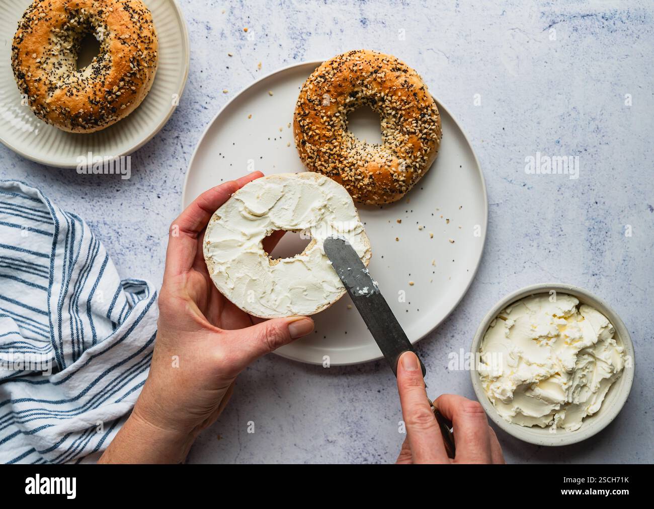 Vue de dessus des mains étalant du fromage à la crème sur tout bagel. Banque D'Images