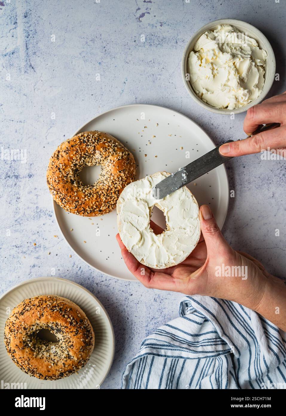 Vue de dessus des mains étalant du fromage à la crème sur tout bagel. Banque D'Images