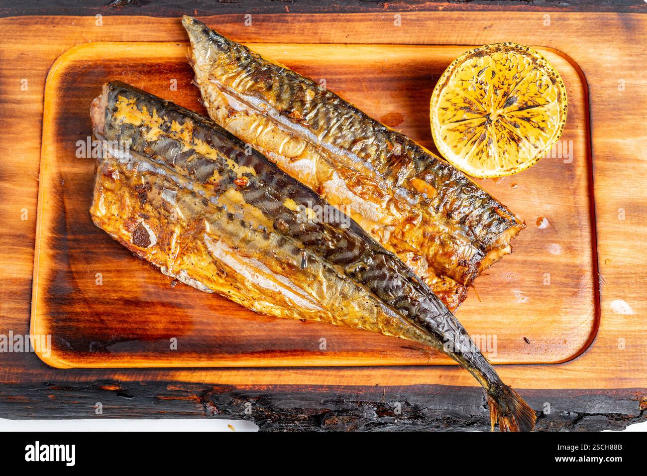 Les filets de maquereau grillés juteux reposent sur une planche de bois accompagnés d'une moitié de citron carbonisé. Ce plat met en valeur la simplicité et la saveur de la seafo fraîche Banque D'Images