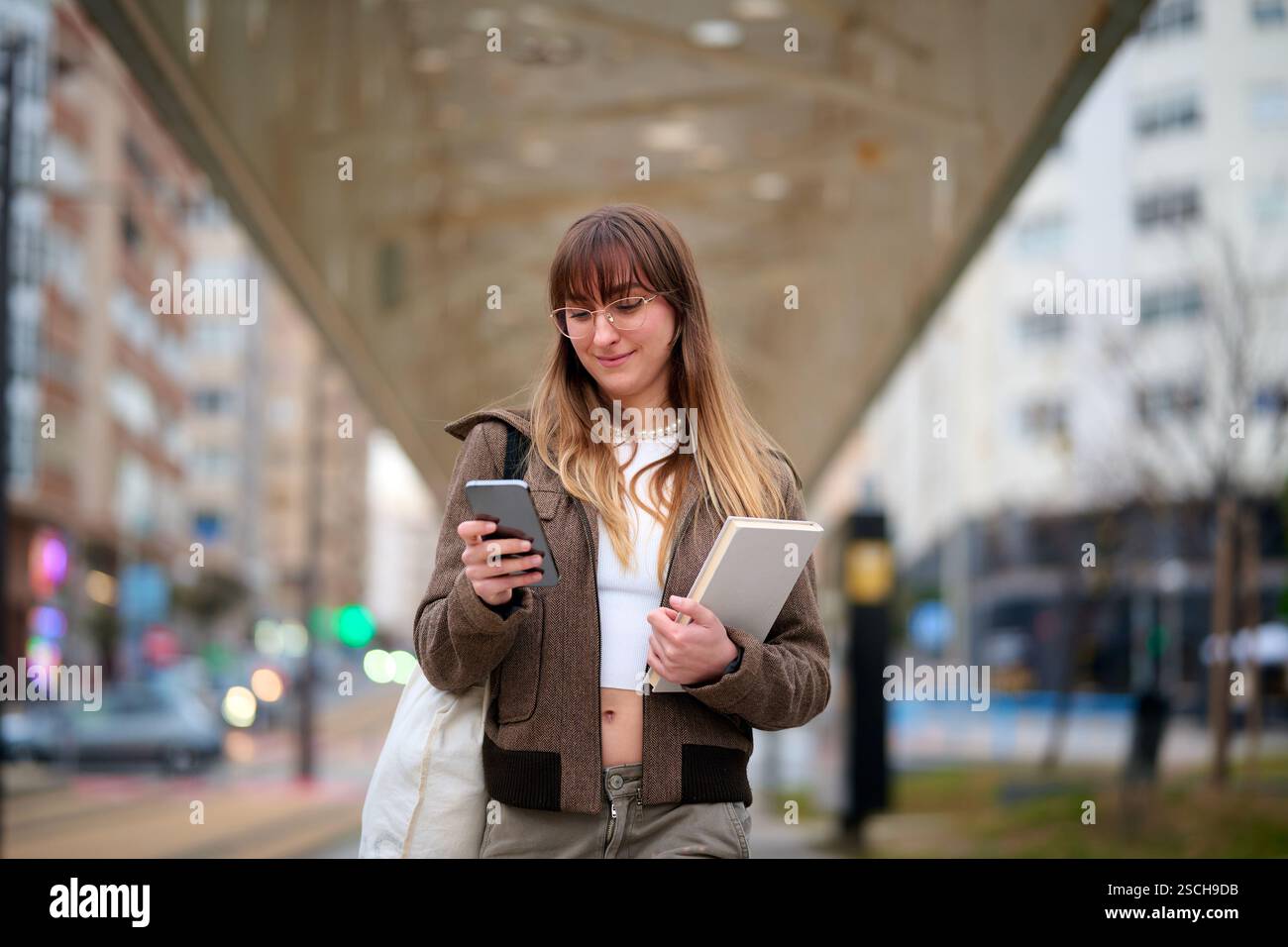 Femme s'engage avec le téléphone tout en tenant le livre à l'emplacement urbain Banque D'Images