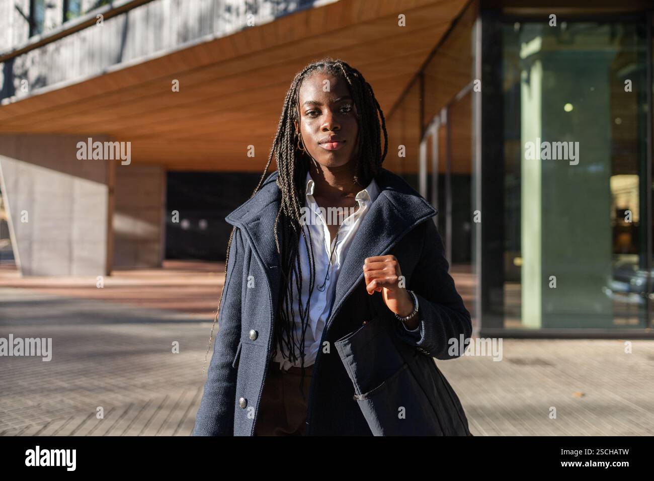 Une femme d'affaires afro-américaine aux cheveux tressés aime une pause à l'extérieur, habillée intelligemment d'un manteau sur une chemise blanche. Banque D'Images