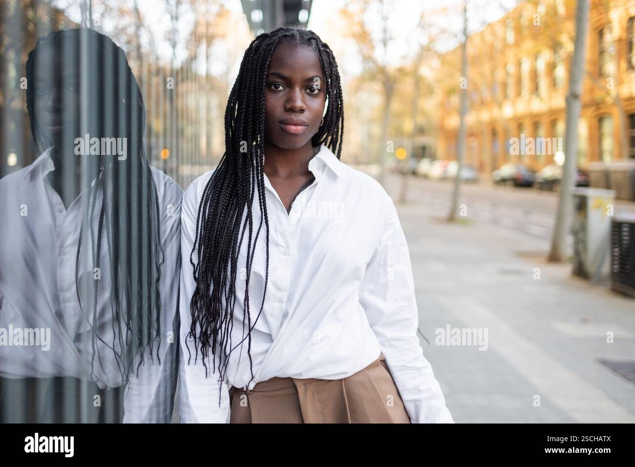 Une femme d'affaires afro-américaine avec des tresses est présentée debout à l'extérieur, portant une chemise blanche formelle et un pantalon kaki, avec un expressio concentré Banque D'Images