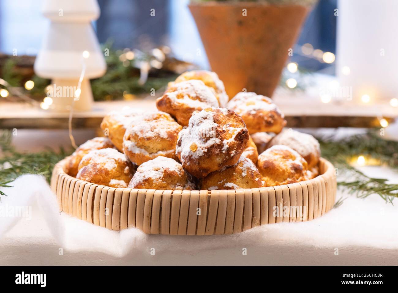 Un panier rempli de délicieuses pâtisseries saupoudrées de sucre en poudre, posé sur une table de fêtes. Le fond est orné de lumières douces et gre Banque D'Images