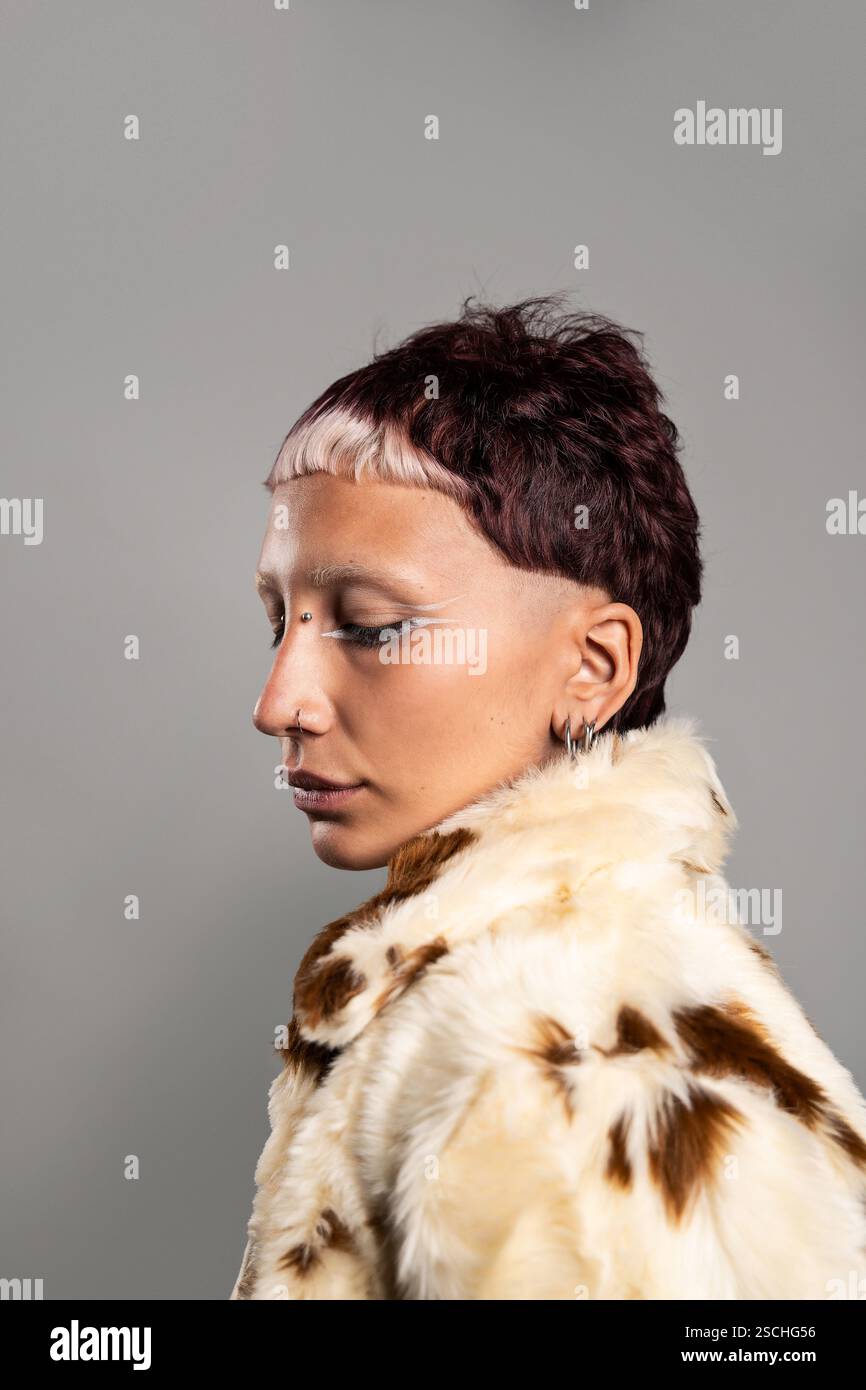 Un portrait de profil saisissant d'une femme aux cheveux courts et foncés et eyeliner géométrique. Ils portent un manteau de fourrure à motifs, mettant en vedette un sty artistique et audacieux Banque D'Images