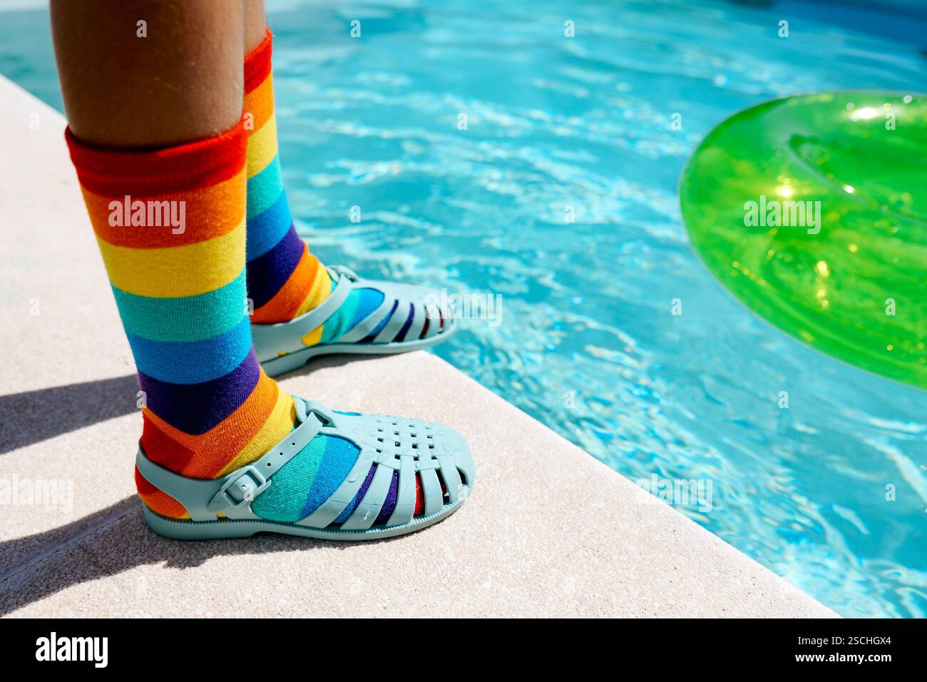 Une scène vibrante avec des chaussettes à rayures arc-en-ciel jumelées à des sandales bleues près d'une piscine lumineuse. Les chaussettes colorées et l'anneau gonflable vert ajoutent un Banque D'Images