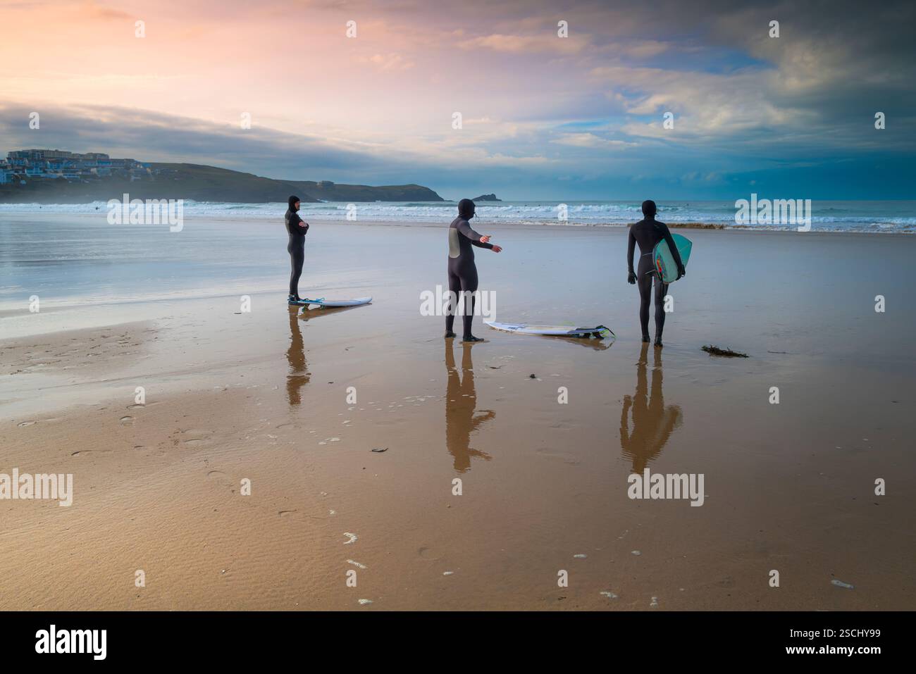 Un groupe de trois surfeurs debout et se préparant pour une séance de surf sur Fistral Beach à Newquay en Cornouailles au Royaume-Uni. Banque D'Images