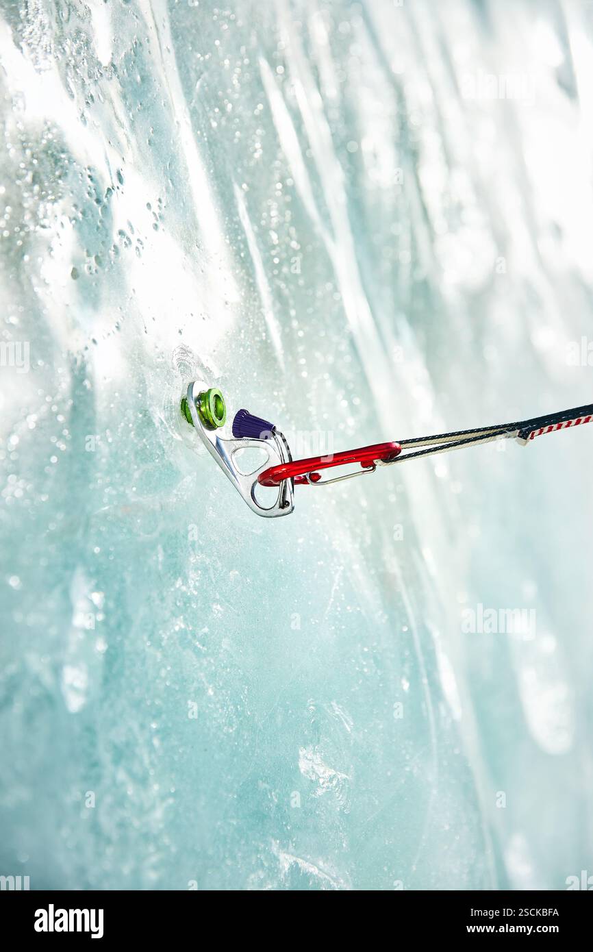 Gros plan mince quickdraw avec mousqueton rouge grimpant accroché les vis à glace annulaires vissées dans la glace d'un mur de glacier gelé. Concept d'équipement d'escalade Banque D'Images