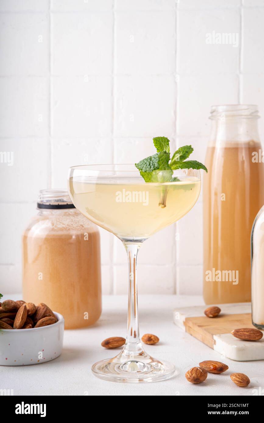 Cocktail d'orgeat au citron aigre-doux, recette de limonade à l'orgeat, un verre à martini avec boisson alcoolisée et bouteille de sirop d'orgeat d'amande Banque D'Images