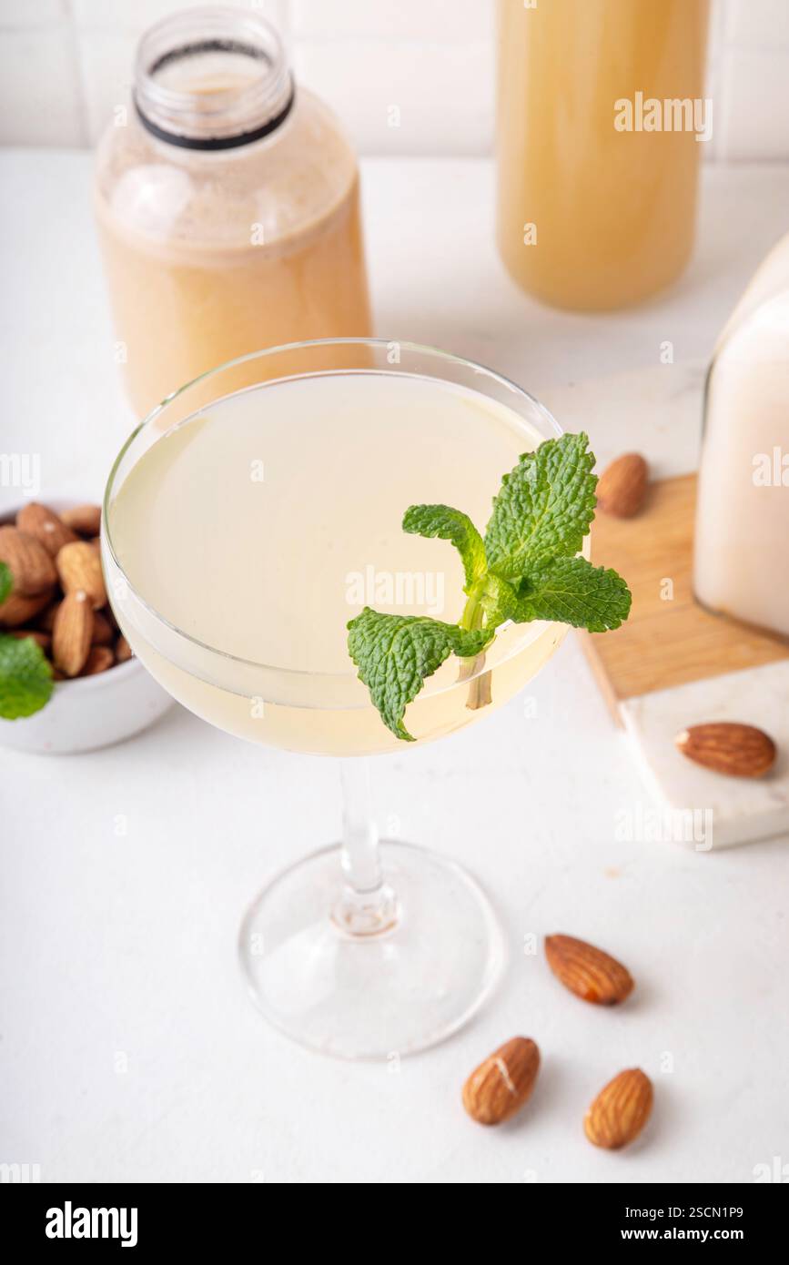 Cocktail d'orgeat au citron aigre-doux, recette de limonade à l'orgeat, un verre à martini avec boisson alcoolisée et bouteille de sirop d'orgeat d'amande Banque D'Images