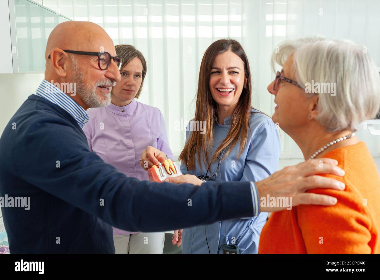 Dentistes discutant d’un modèle de prothèse avec un couple de personnes âgées lors d’une consultation dans un environnement de clinique dentaire accueillant Banque D'Images