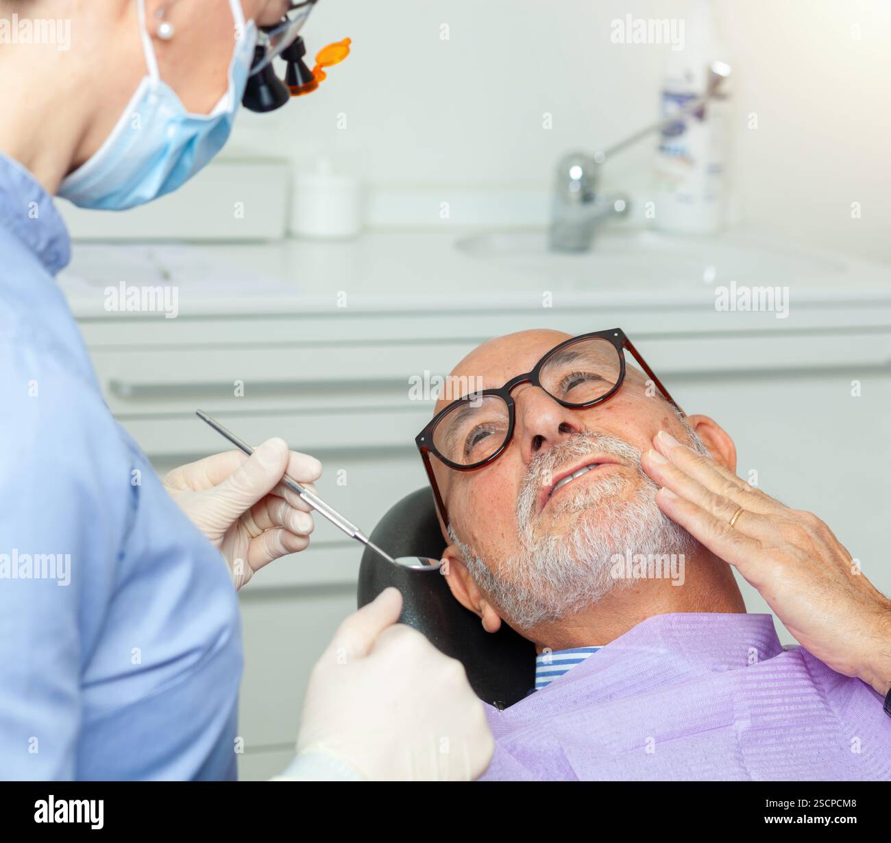 Homme âgé éprouvant des maux de dents lors d'un examen dentaire, montrant des signes d'inquiétude tout en subissant un examen dans une clinique Banque D'Images