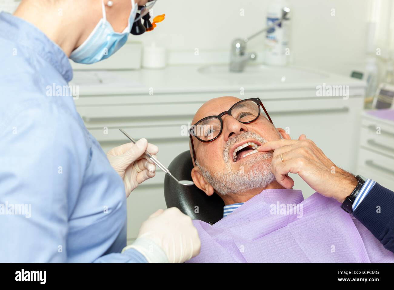 Dentiste portant un masque chirurgical et utilisant des outils dentaires examinant un homme d'affaires senior avec mal de dents dans une clinique dentaire brillante Banque D'Images