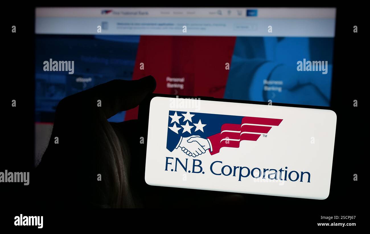Dans cette illustration photo, une personne tient un téléphone portable avec le logo de la société américaine FNB Corporation (First National Bank) sur l'écran devant la page Web. Banque D'Images