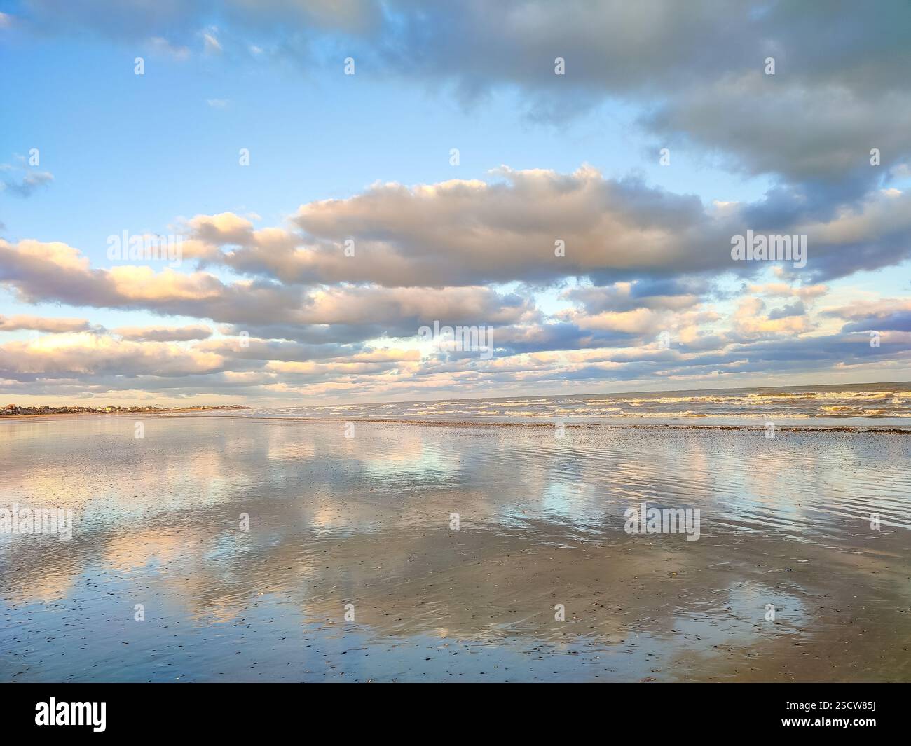 Des teintes douces remplissent le ciel au-dessus des eaux tranquilles tandis que le soleil se couche le long de la plage de sable. Banque D'Images