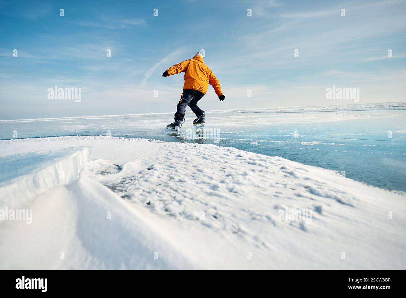 Homme athlète en veste jaune patin sur glace sur le lac gelé avec des fissures et de la neige à l'heure d'hiver Banque D'Images