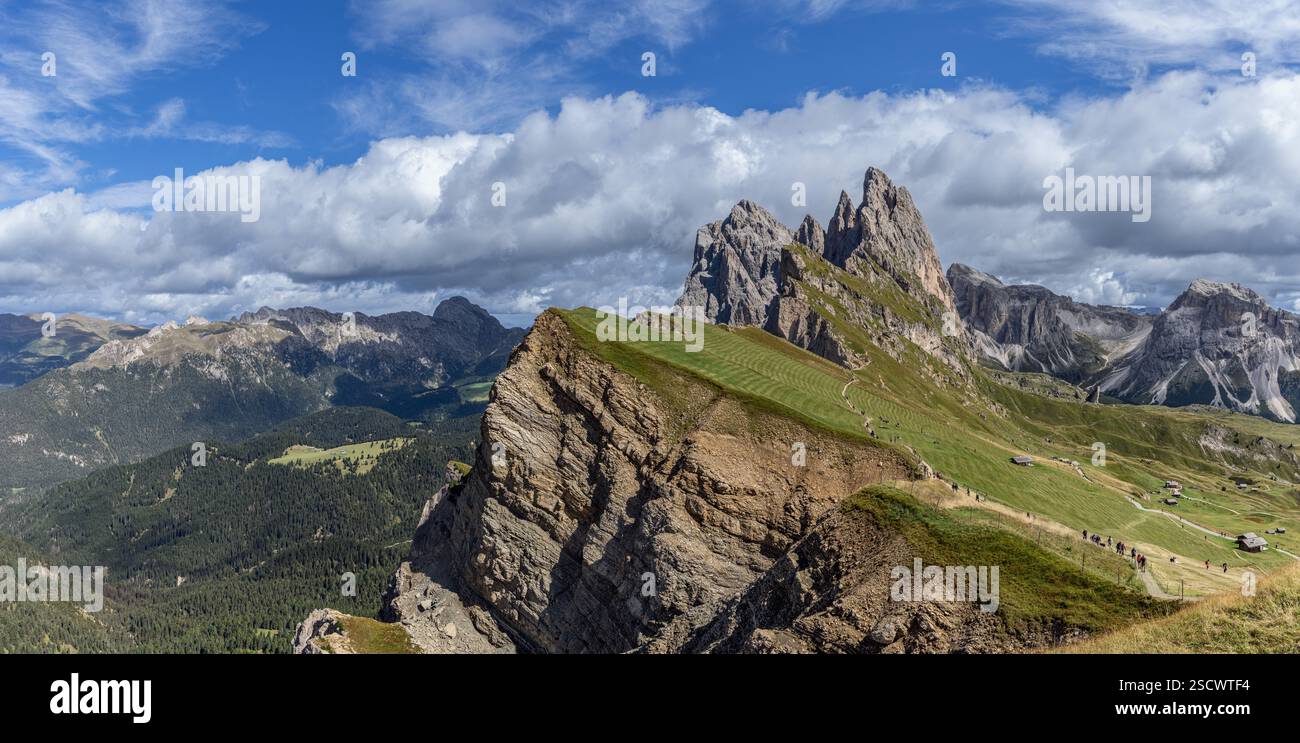 Large vue panoramique de Seceda, un lieu de photo renommé dans les Dolomites, Italie, avec un plateau herbeux, des falaises abruptes, des sommets montagneux et des touristes e. Banque D'Images