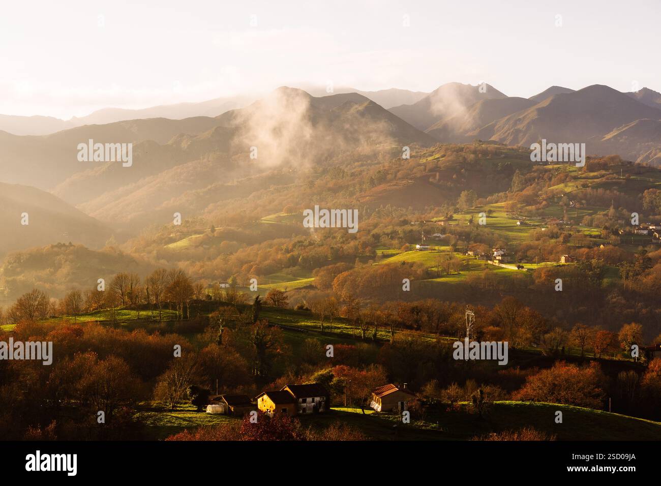 Lever de soleil brumeux sur une vallée aux couleurs d'automne, maisons dispersées sur les collines, et montagnes en arrière-plan. Banque D'Images