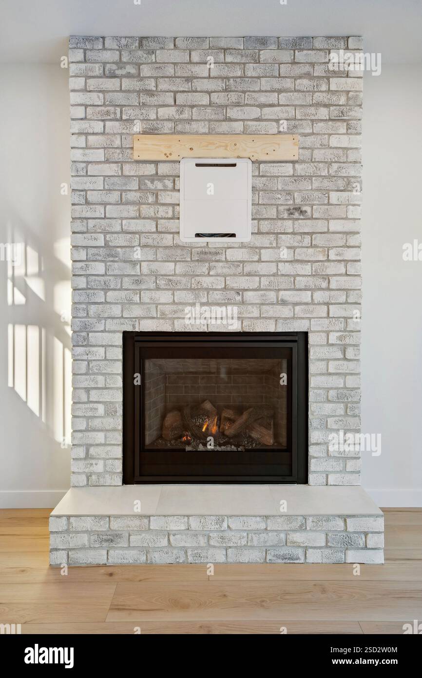 Manteau de cheminée en brique avec une boîte blanche sur le dessus. La boîte est blanche et a un cadre noir. La cheminée est noire et a une porte vitrée. La chambre est bien Banque D'Images