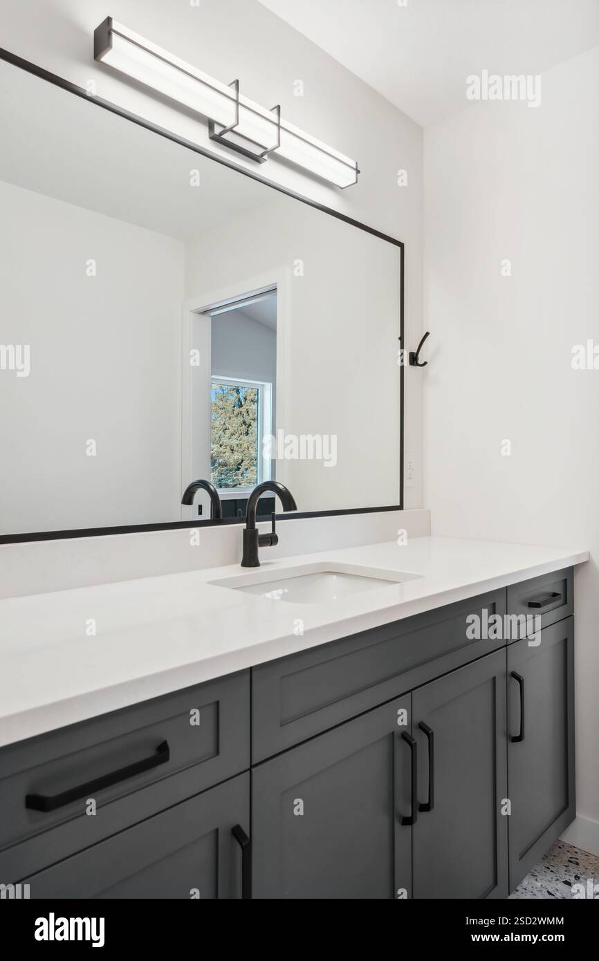 Salle de bains avec lavabo noir et miroir noir. La salle de bain est propre et bien éclairée, avec un comptoir blanc et des armoires noires. L'évier est positionné Banque D'Images