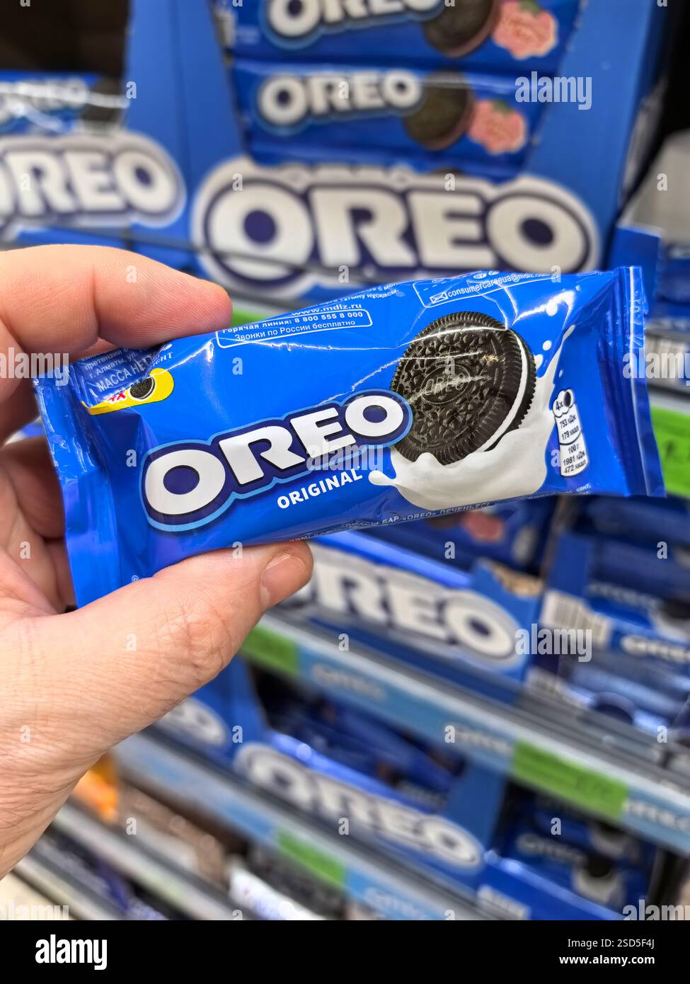 Bobruisk, Biélorussie - 4 février 2025 : une personne tient un paquet de gâterie classique avec une garniture de crème, entouré d'étagères remplies de collation similaire Banque D'Images