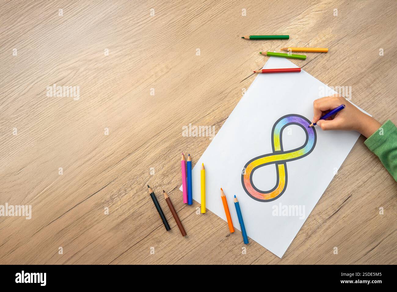 Une main coloriant un symbole d'infini arc-en-ciel sur une feuille de papier blanche avec des crayons de couleur dispersés autour. Concept de sensibilisation à l'autisme. Banque D'Images Une main coloriant un symbole d'infini arc-en-ciel sur une feuille de papier blanche avec des crayons de couleur dispersés autour. Concept de sensibilisation à l'autisme. Banque D'Images