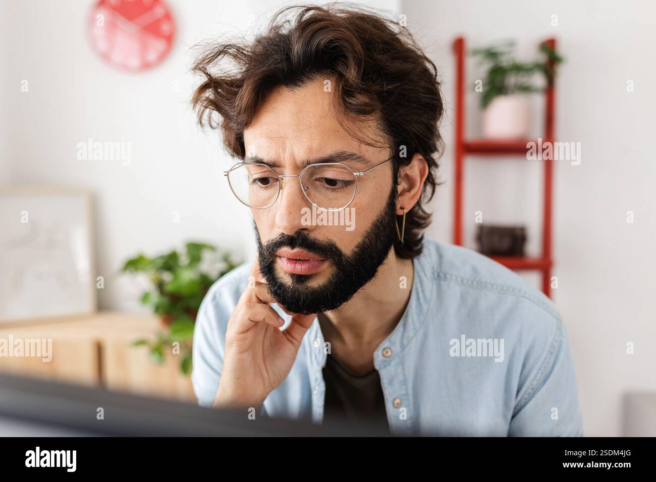 Jeune homme adulte regardant l'écran d'ordinateur tout en travaillant à la maison Banque D'Images Jeune homme adulte regardant l'écran d'ordinateur tout en travaillant à la maison Banque D'Images