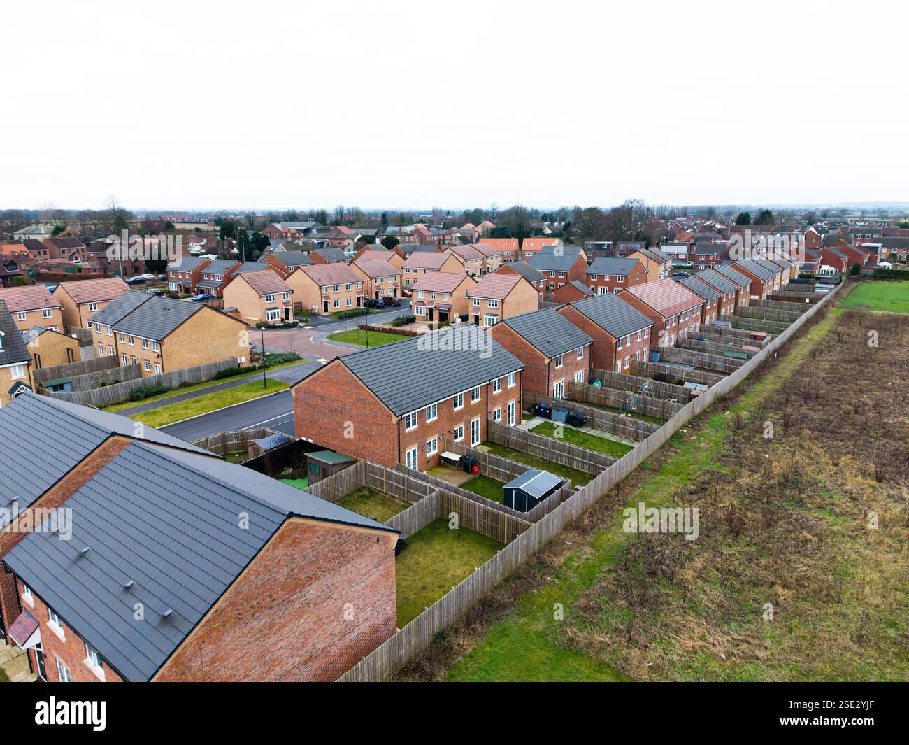 Vue panoramique aérienne d'une rangée de maisons neuves sur le bord d'un village britannique. Maisons abordables construites sur des terres de la ceinture verte augmentant la population du village Banque D'Images