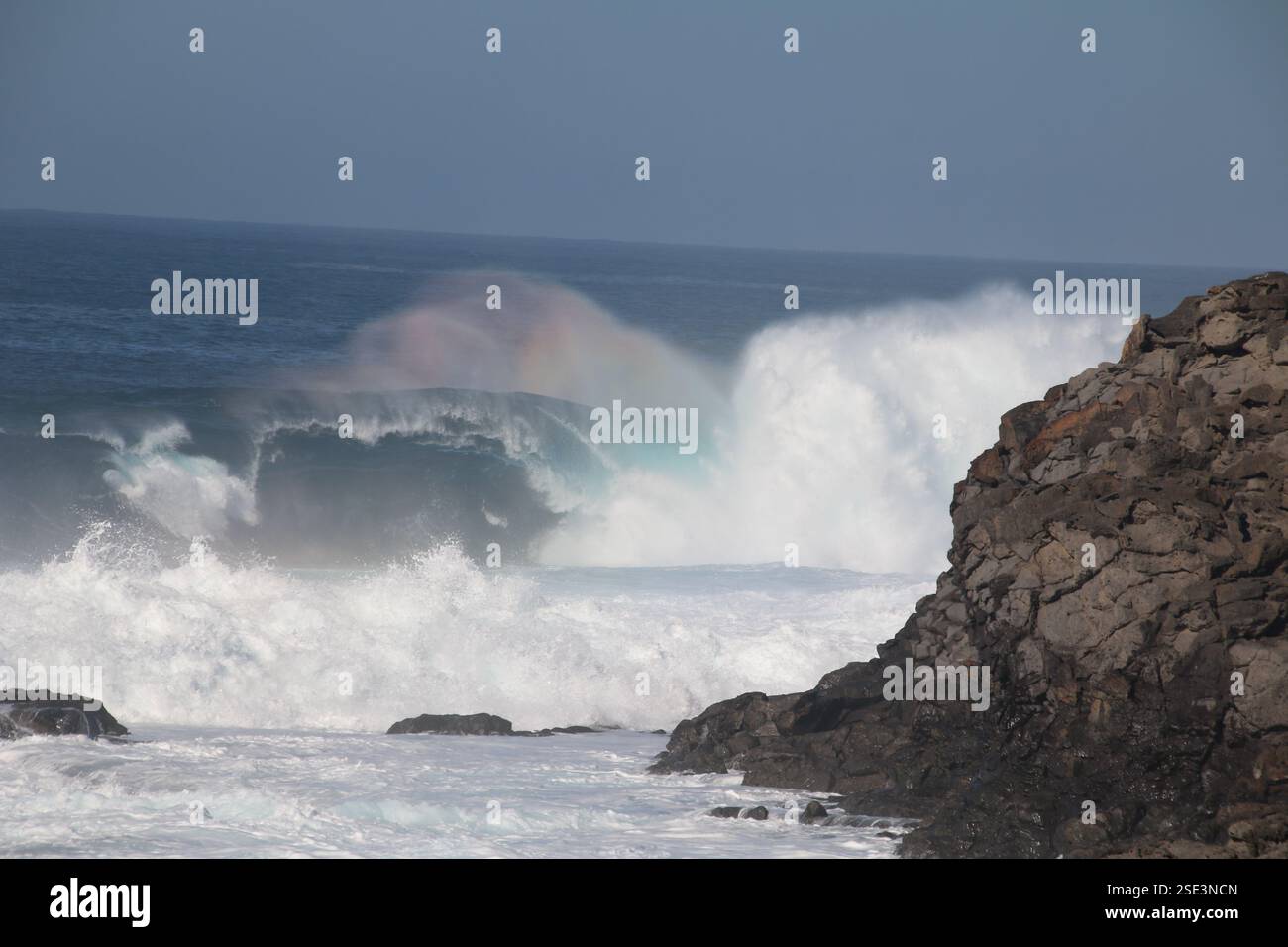 vagues de mer agitées s'écrasant sur les rochers causant l'effet arc-en-ciel Banque D'Images