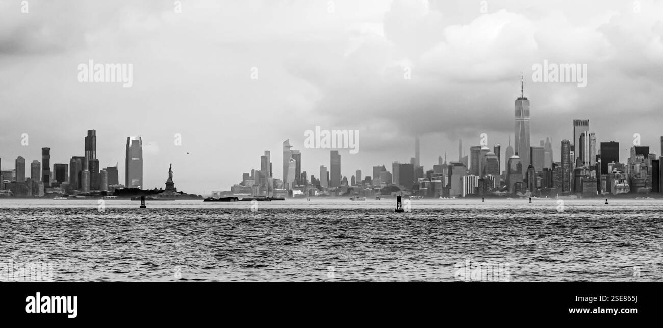 La ligne d'horizon de New York domine l'eau, avec la Statue de la liberté bien en vue au premier plan sous un ciel nuageux spectaculaire. Le ur Banque D'Images