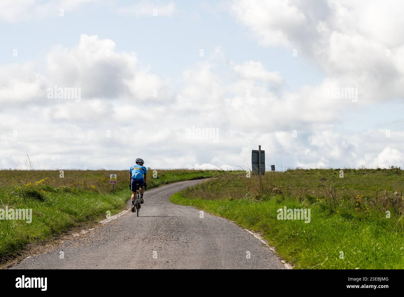 Un cycliste passe devant des panneaux d'avertissement sur une route traversant les Imber Ranges, la zone d'entraînement de l'armée britannique sur la plaine de Salisbury dans le Wiltshire, en Angleterre. Banque D'Images
