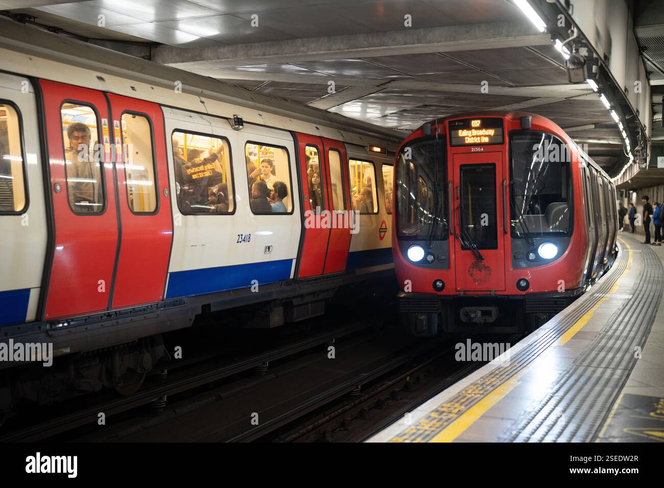 Métro de Londres District Line à la station Edgware Road. Deux trains, un rouge, un blanc/rouge, sont visibles. Les navetteurs sont à bord. Banque D'Images