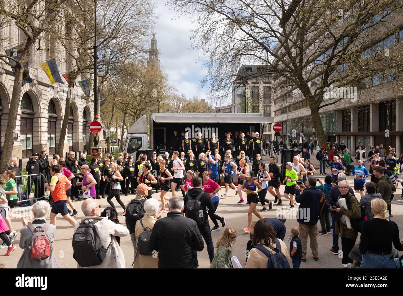 Coureurs dans une course près de Strand Aldwych à Londres. Un grand groupe de personnes participent à une course, avec une chorale sur une scène. Banque D'Images