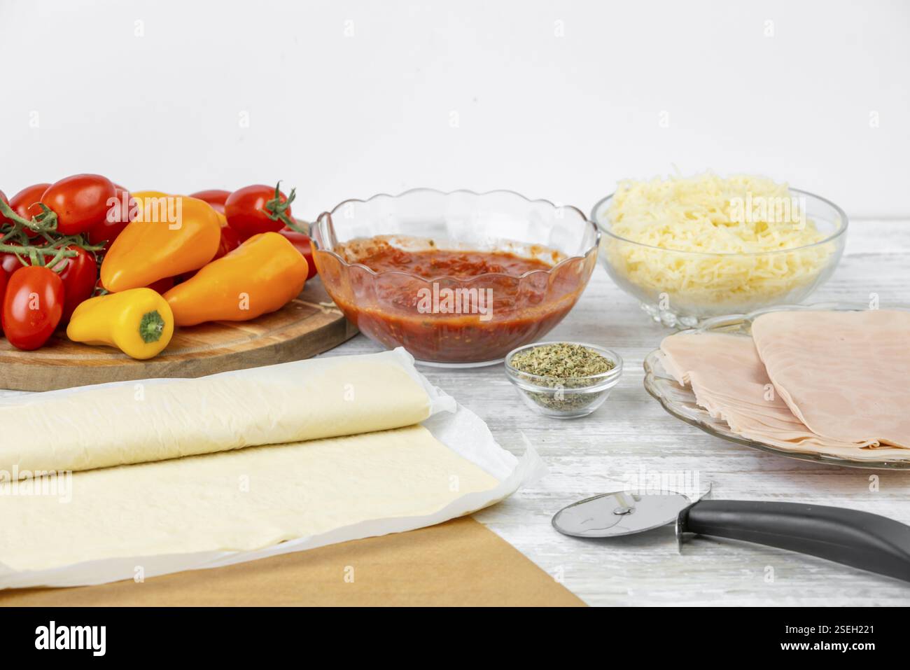 Ingrédients de cuisson, tomates, poivrons, sauce tomate, fromage, jambon et pâte à pizza Banque D'Images