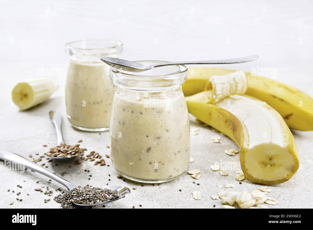 Milk-Shake avec des graines de chia, des graines de lin, des flocons d'avoine, du riz soufflé et de la banane dans deux pots en verre sur un fond de table en granit Banque D'Images