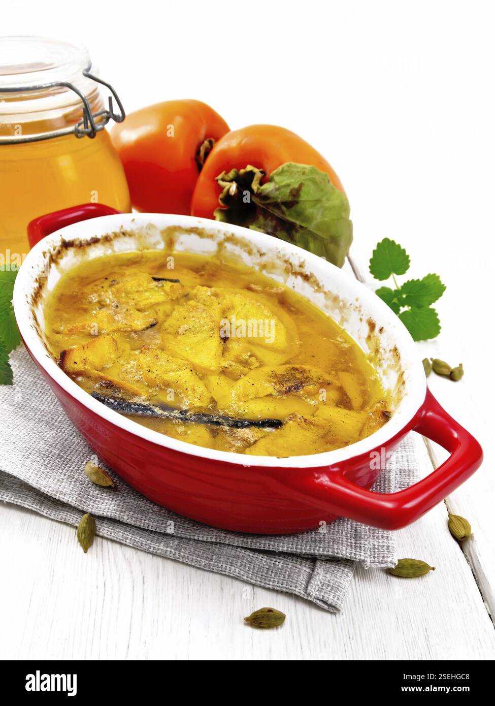 Persimmon cuit au miel, à la cardamome et à la vanille dans une rôtissoire sur une serviette, menthe et fruit orange sur fond de bois Banque D'Images
